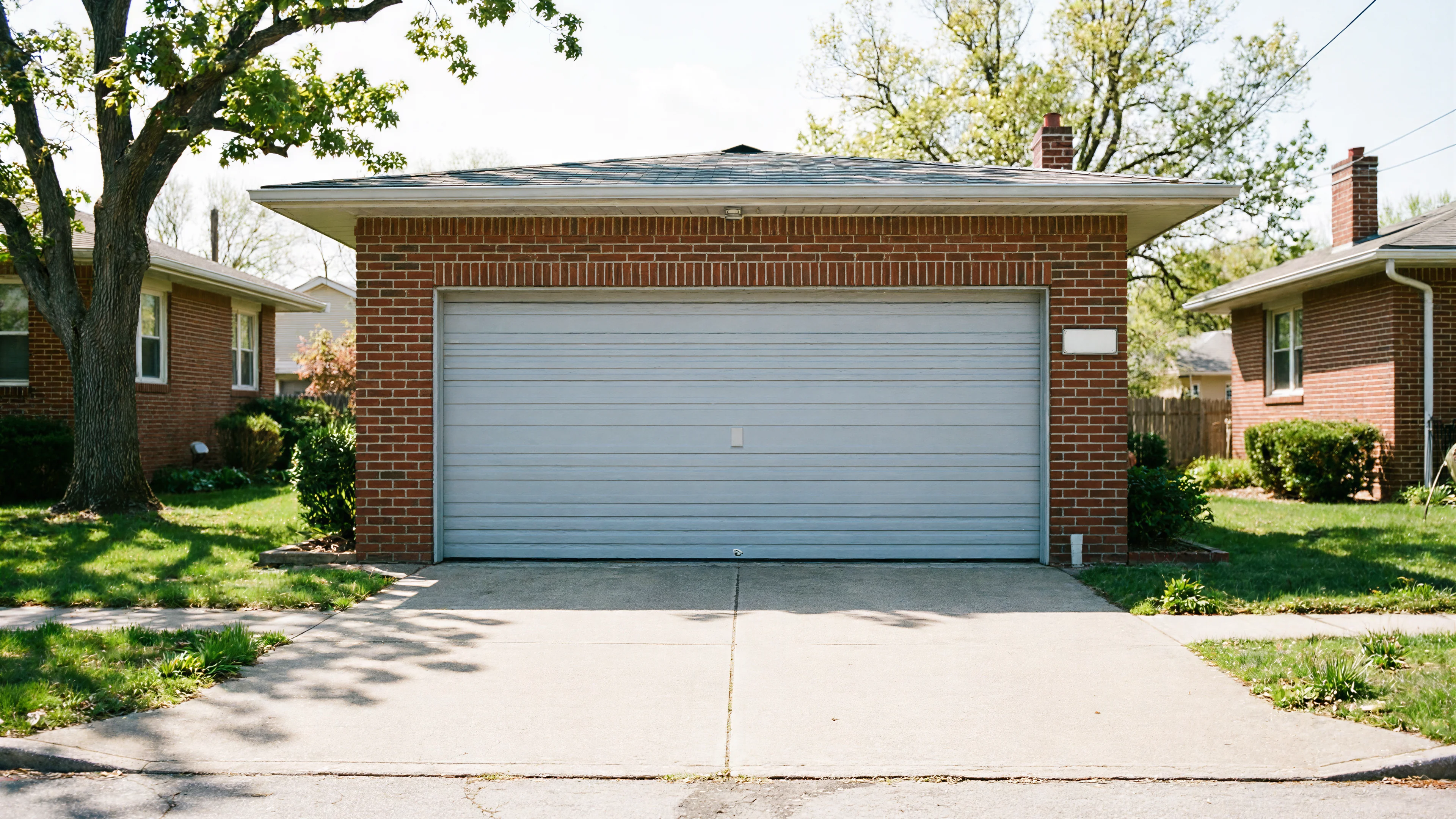 A brick garage with a light gray garage door and concrete driveway.